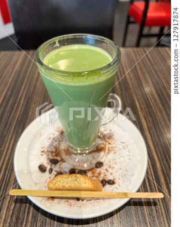 Green beverage served in a tall glass on a white plate with a cookie and coffee beans, showcasing a delightful cafe experience 127917874