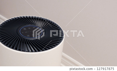 Tall round air purifier with a black top fan and a white body on a tile floor against the wall 127917875
