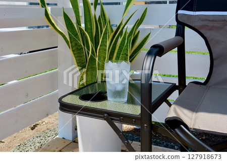 A glass of ice and water placed on a chair side table with a white wooden fence in the background A glass of ice and water placed on a chair side table with a white wooden fence in the background 127918673