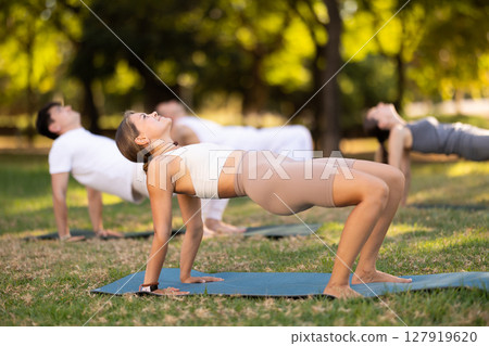Yoga lesson visitors with girl coach perform crab pose in park 127919620
