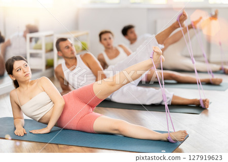 Young girl practicing leg lift with band on feet lying on the side 127919623