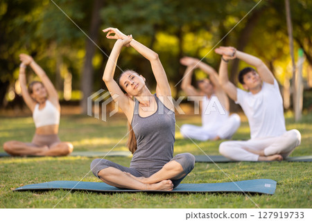 Yoga lesson visitors with girl coach perform padmasana in park 127919733