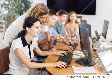 Interested girl attending computer class under guidance of male teacher 127919735