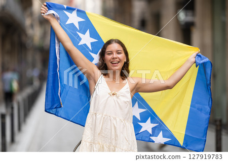 Woman waving flag of Bosnia and Herzegovina flag on street of summer European city 127919783
