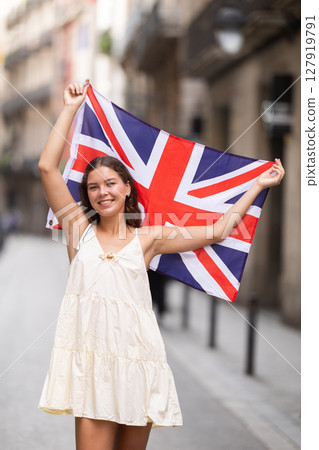 Cheerful girl holding national flag of UK flag, standing outdoors 127919791