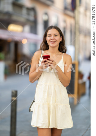 Young woman with phone walking along city street 127919793