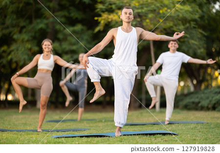 Man performing one-legged pose during group yoga in summer park 127919828