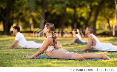 Yoga lesson visitors with coach perform dog face up and cobra pose in park Yoga lesson visitors with coach perform dog face up and cobra pose in park 127919849