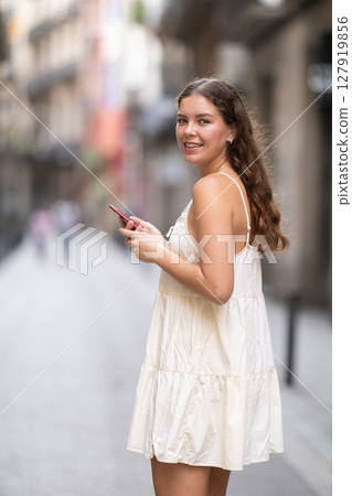 Young woman with phone walking along city street 127919856