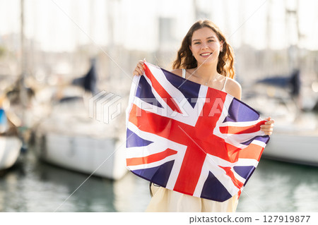 Woman waving national flag of UK against seaport and yachts Woman waving national flag of UK against seaport and yachts 127919877