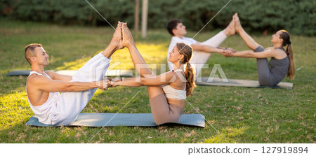 Guy and girl practice pair yoga doing Buddy boat pose asana Guy and girl practice pair yoga doing Buddy boat pose asana 127919894