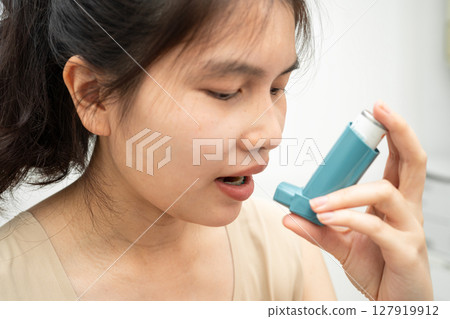 Asthma and chronic obstructive pulmonary disease COPD, Asian woman using metered dose inhaler MDI. 127919912