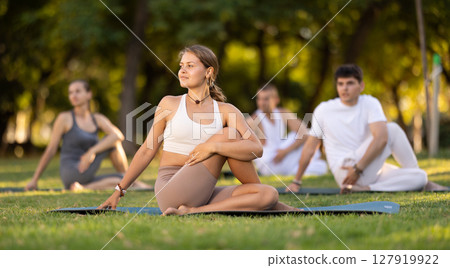 Yoga lesson visitors with coach perform Matsyendrasana in park 127919922
