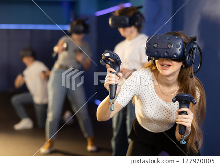 Excited young woman in VR goggles having fun in virtual reality room 127920005