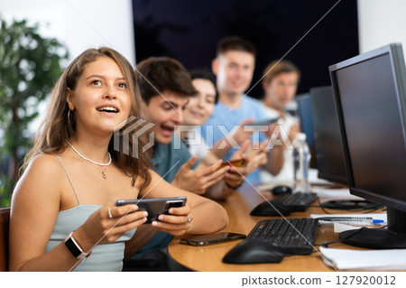 At computer class, young girl student sits with mobile phone and listens admiringly to teacher At computer class, young girl student sits with mobile phone and listens admiringly to teacher 127920012