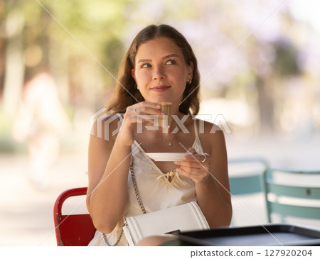 Smiling woman drinking espresso coffee while sitting on terrace of street cafe Smiling woman drinking espresso coffee while sitting on terrace of street cafe 127920204