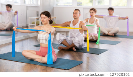 Young men and women doing arm workout with band sitting cross-legged Young men and women doing arm workout with band sitting cross-legged 127920301