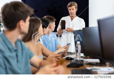 During computer courses, male teacher with mobile phone explains to listeners principle of operation 127920306