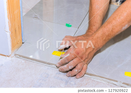 Hands of worker carefully placing tiles on floor in home renovation project. 127920922