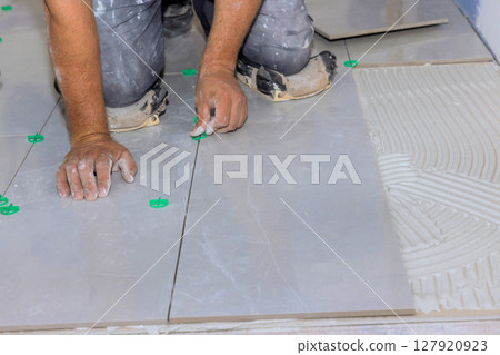 Worker meticulously places tiles on floor, ensuring precision careful alignment in renovation setting. 127920923