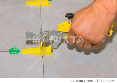 Hand operated tile leveling device on gray flooring while installing tiles in home improvement project. 127920926