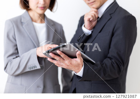 A middle-aged male businessman and female businesswoman in suits looking at a tablet and worrying 127921087