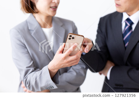 A middle-aged male businessman and female businesswoman in suits looking at their smartphone and worrying A middle-aged male businessman and female businesswoman in suits looking at their smartphone and worrying 127921356