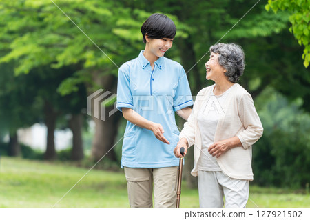 Senior woman using a walking stick and her caregiver 127921502