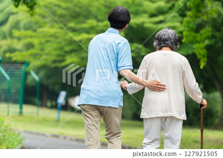 一位拄著拐杖的老年婦女和她的護理人員的後視圖 127921505