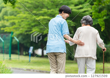 Rear view of a senior woman using a cane and her caregiver 127921509