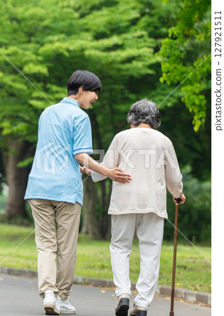 Rear view of a senior woman using a cane and her caregiver 127921511