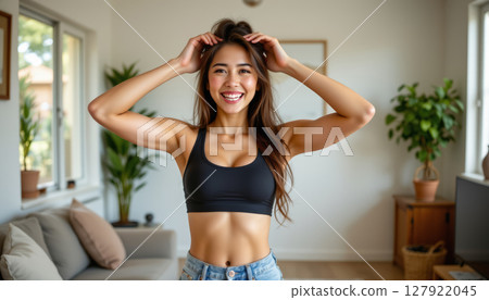 Young woman smiling in cozy living room, showcasing fitness and confidence 127922045