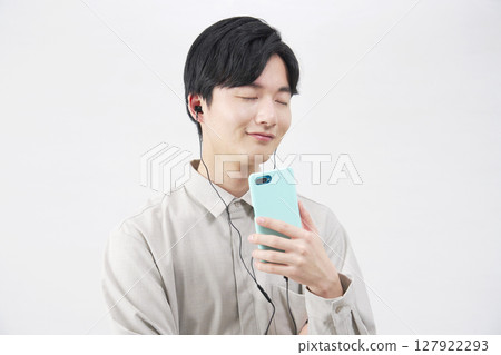 A man in his 20s listening to music with earphones on a white background A man in his 20s listening to music with earphones on a white background 127922293