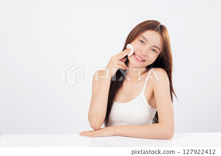 Cotton pad helps this Asian woman gently use cotton to cleanse her skin, removing makeup from her face with a happy and refreshed expression. isolated studio white background Cotton pad helps this Asian woman gently use cotton to cleanse her skin, removing makeup from her face with a happy and refreshed expression. isolated studio white background 127922412