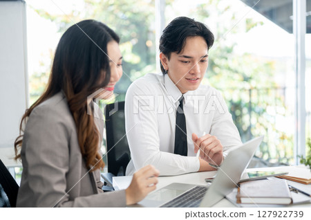 Female office worker and her male coworker is smiling while talking together at the working desk. Female office worker and her male coworker is smiling while talking together at the working desk. 127922739
