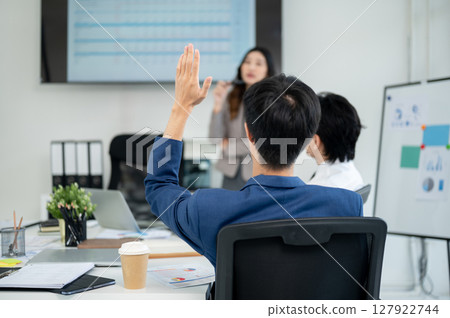 Businessman or male office worker raising a hand to ask a question with female coworker during a meeting Businessman or male office worker raising a hand to ask a question with female coworker during a meeting 127922744