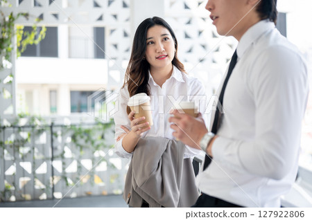 An asian female office worker and male coworker is holding coffee cup while chatting together. 127922806