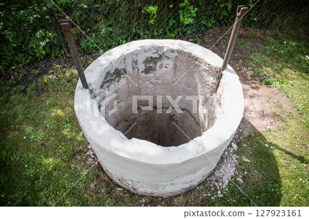 Open Concrete Water Well on Grass Yard Under Sunlight with Iron Support Bars Open Concrete Water Well on Grass Yard Under Sunlight with Iron Support Bars 127923161