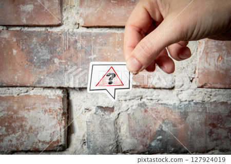 Question Mark Warning Symbol Concept Held by Hand Against Brick Wall Background 127924019