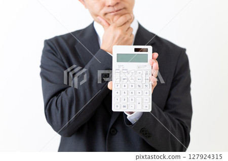 A middle-aged male businessman in a suit holding a calculator and worrying A middle-aged male businessman in a suit holding a calculator and worrying 127924315