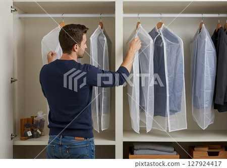 Man hanging clothes in breathable garment bags for moth protection 127924417