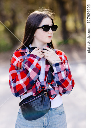 Young stylish woman adjusting headphones while listening to music outdoors 127924603
