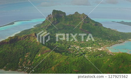 Lush vegetation covers almost entirely mount otemanu, the highest point of bora bora island, while turquoise waters lap against the sandy shores below 127925562