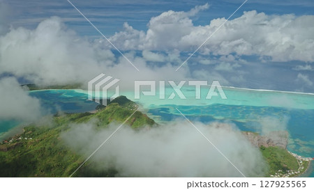 Clouds covering turquoise lagoon of Bora Bora tropical island, with its lush green motus mountains and coral reefs visible from aerial perspective, showcasing the tropical beauty of French Polynesia 127925565