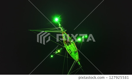 Green lights from a squid fishing boat create a mesmerizing spectacle in the dark waters near Koh Phangan, Thailand, offering a unique perspective on traditional fishing practices 127925581