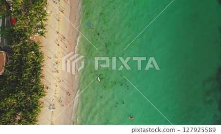 Cagban Beach in Boracay, Philippines, seen from above, with tourists swimming, sunbathing, and enjoying the tropical paradise, surrounded by palm trees and crystal-clear turquoise waters 127925589