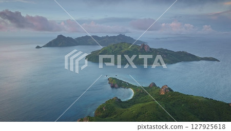 Capturing aerial drone footage of Fiji islands during sunset, showcasing lush green hills, vibrant turquoise waters, and dramatic sky filled with pink and grey clouds. Amazing nature travel background Capturing aerial drone footage of Fiji islands during sunset, showcasing lush green hills, vibrant turquoise waters, and dramatic sky filled with pink and grey clouds. Amazing nature travel background 127925618