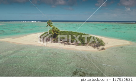 Aerial view of a small desert island with palm trees and lush vegetation surrounded by a turquoise lagoon and coral reef in French Polynesia, a dream destination for vacations and relaxation 127925621