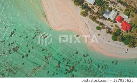 Aerial view capturing a lonely boat floating gracefully near a stunning tropical island, featuring charming houses, swaying palm trees, and inviting transparent turquoise waters 127925623