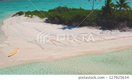 Sandy message, word TRAVEL written on picturesque sand beach, yellow kayak rests nearby, pristine turquoise water, lush greenery. Remote wild nature paradise, exotic summer holidays. Aerial panorama 127925634